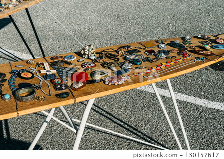 Assorted vintage jewelry including brooches, necklaces, and bold accessories displayed on a wooden table outdoors. Retro glam, flea market finds, maximalist fashion, secondhand style 130157617