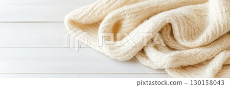 Cozy cream-colored knitted blanket placed on a light wooden surface for a serene interior setting 130158043