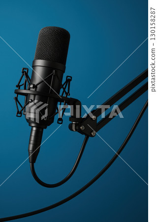 Professional studio microphone with shock mount and adjustable arm setup for podcasting and broadcasting, isolated on blue background with clear focus and high resolution 130158287