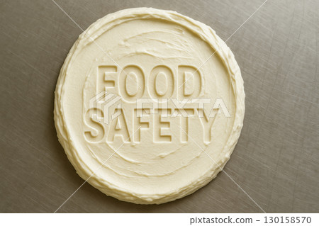Cream cheese spread with words food safety embossed on its smooth surface on stainless steel inspection table, emphasizing hygiene and quality control in food production 130158570