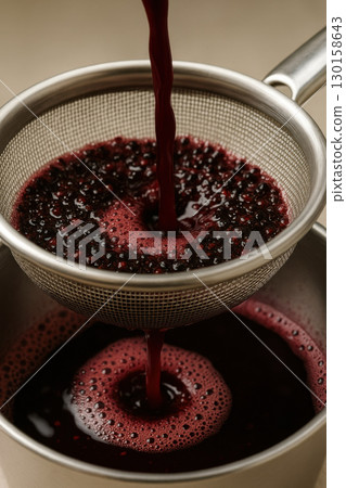 Dark berry juice pouring through metal strainer with seeds winemaking filtration process close up, rich color and texture captured vividly 130158643