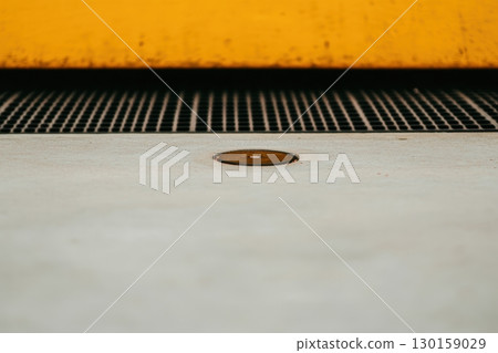 Close-up view of a metal circle on a concrete surface beneath a bright yellow structure in an urban environment 130159029