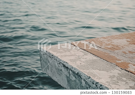 Calm waters reflect the weathered edges of a rustic dock at sunset in a tranquil lakeside setting 130159083