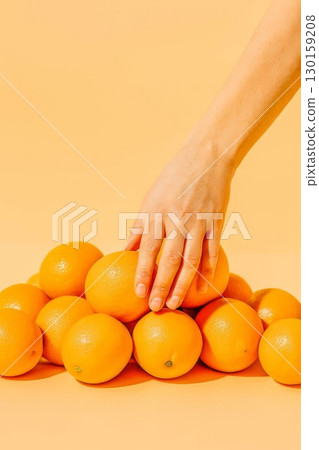Hand picking orange from pile of fresh oranges on orange background. Concept of healthy eating and freshness. 130159208