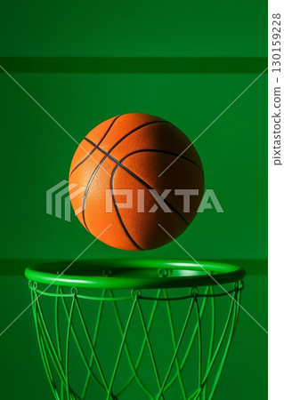 Basketball ball flying over green hoop on vibrant background. Minimalist sports concept, dynamic composition, athletic 130159228