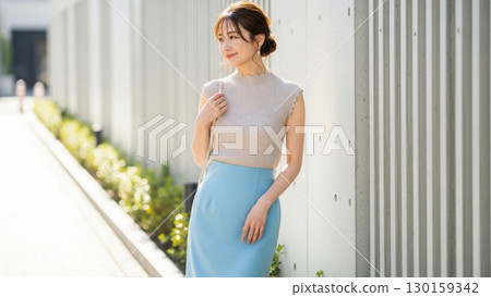 一位 40 多歲的美女在牆邊微笑，沐浴著夏日的陽光 130159342