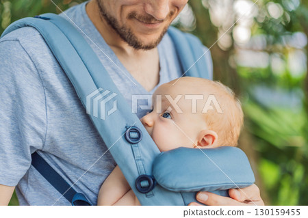 Young father walks in nature with his baby son nestled close in a parent-facing ergonomic baby carrier. Bonding, warmth, and modern parenting concept in a peaceful outdoor setting Young father walks in nature with his baby son nestled close in a parent-facing ergonomic baby carrier. Bonding, warmth, and modern parenting concept in a peaceful outdoor setting 130159455