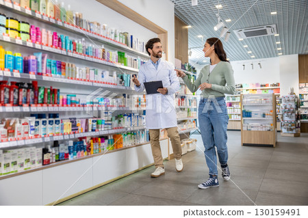 Pharmacy assistant with a notepad in hands talking to a female client 130159491