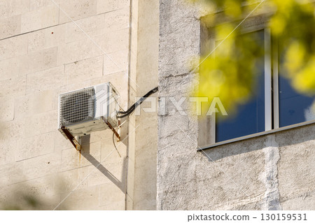 air conditioner on wall of an apartment building with view of green trees. air conditioner on wall of an apartment building with view of green trees. 130159531