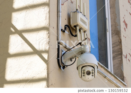 Camera is mounted on a wall. The camera is white and has a black lens Camera is mounted on a wall. The camera is white and has a black lens 130159532
