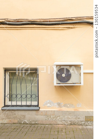 air conditioner in an anti-vandal grid is installed on wall of house.  130159534