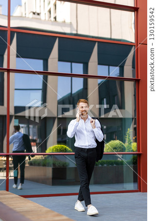 Stylish redhead in formal attire communicating on smartphone while walking Stylish redhead in formal attire communicating on smartphone while walking 130159542