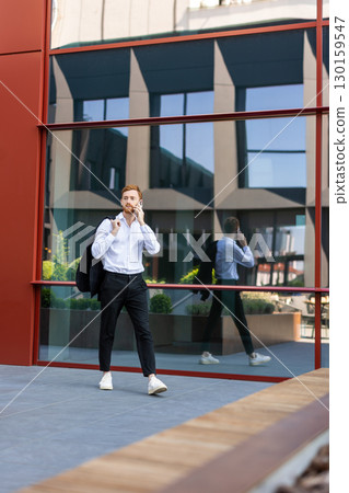 Red-haired man in white shirt talking on smartphone in modern city environment 130159547