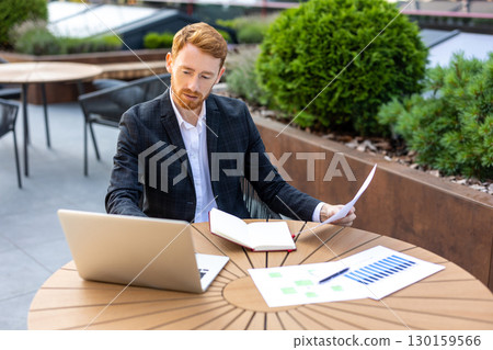 Caucasian businessman combining laptop work with paper files 130159566