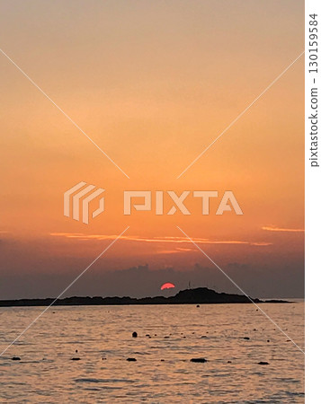 Sunrise over the sea with small island silhouette, golden sky and sun reflection on water, tranquil seascape at dawn 130159584