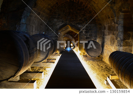 A historic wine cellar with an antique wooden press, grape crusher, and giant barrel. The concept is traditional winemaking heritage and craftsmanship. 130159854