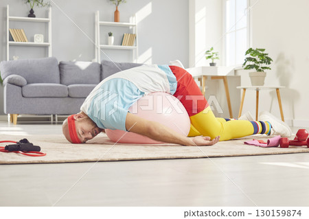 A funny tired man is lying on a fit ball on the floor with closed eyes after fitness workout. 130159874