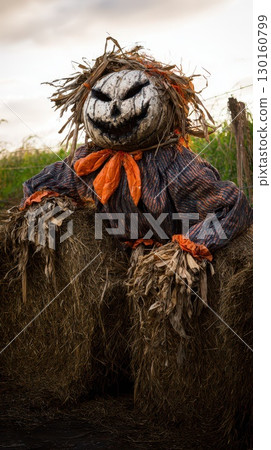 Creepy scarecrow sitting on hay bales at dusk 130160799