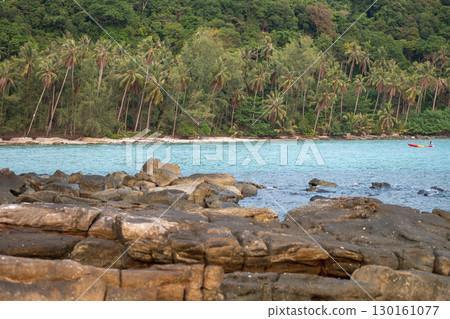 Rocky shoreline with tropical forest and boat on calm sea water 130161077