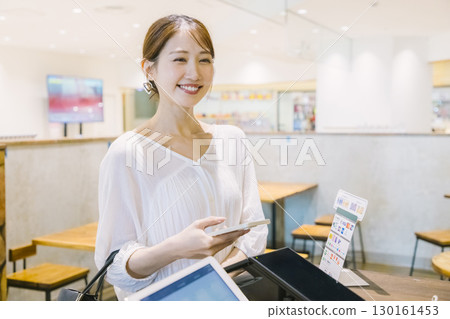 A woman making a cashless payment at a cafe register 130161453