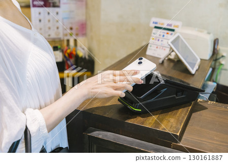 A woman making a cashless payment at a cafe register 130161887