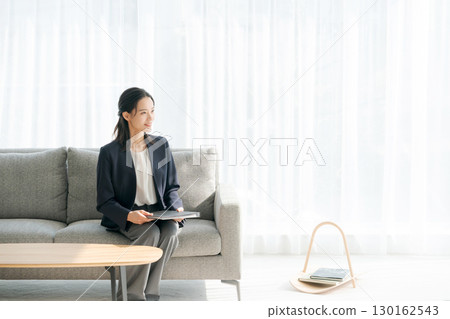 A woman in a suit sitting on a sofa in the living room 130162543