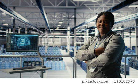 Portrait of smiling IT professional in server farm optimizing machine learning systems handling tasks. Happy data center female engineer adjusting neural networks AI model parameters, camera A 130162579