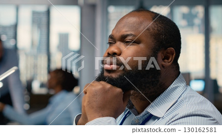 Close up of trader daydreaming, visualizing becoming rich after stock market speculations. African american man in prop firm office lost in thought, picturing prosperous trade Close up of trader daydreaming, visualizing becoming rich after stock market speculations. African american man in prop firm office lost in thought, picturing prosperous trade 130162581