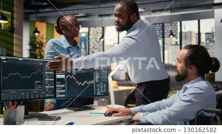 Portfolio manager in wheelchair and coworkers analyze stock market to enhance investment returns. Man with disability and colleagues in inclusive office identify investment opportunities 130162582