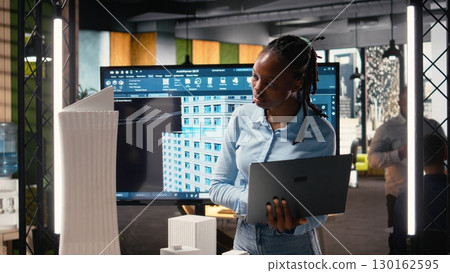 African american female evaluating 3D building model for measurements, creating construction blueprints for layout and preparing documentation for approval on a residential project. 130162595