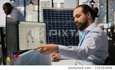 RD department researcher looking over documentation files to study solar green energy systems. Engineer using CAD software on PC to improve photovoltaics carbon footprint, camera B 130162606