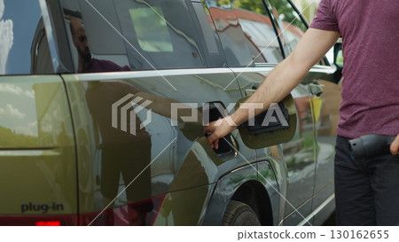 Driver leaving electric SUV car plugged into charger while going to work, reducing greenhouse gas emissions. Man parking green EV vehicle on driveway to get charged at station Driver leaving electric SUV car plugged into charger while going to work, reducing greenhouse gas emissions. Man parking green EV vehicle on driveway to get charged at station 130162655
