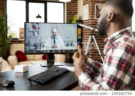 African american self employed man sits at home office desk, having virtual meeting with white male physician on desktop pc. Medical video call focuses on health advice and potential treatment options 130162750