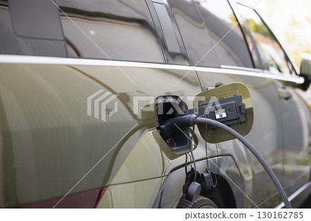 Close up shot of EV plug connected to electric car, concept of eco friendly technology. Electric SUV automobile charging at modern station, showcasing clean energy transportation Close up shot of EV plug connected to electric car, concept of eco friendly technology. Electric SUV automobile charging at modern station, showcasing clean energy transportation 130162785