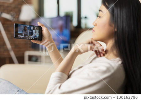 Young female freelancer participating in group video call with multiethnic team. Self employed woman using smartphone for virtual conference, networking with diverse business people. 130162786