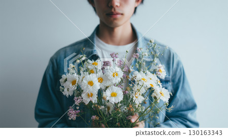 A man holds a bouquet of wildflowers in front of his chest with both hands indoors A man holds a bouquet of wildflowers in front of his chest with both hands indoors 130163343