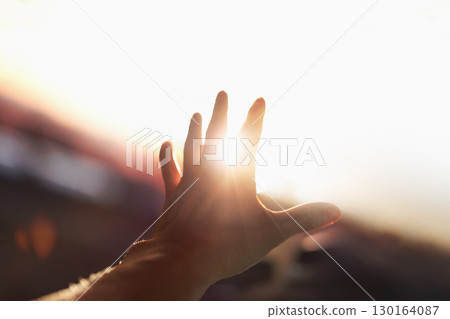 A strong, brilliant beam of light shining through the arms and fingers stretched out toward the bright sun. 130164087