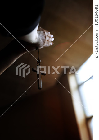 The hands of a Christian holding the cross of Jesus Christ in a church and praying with both hands together 130164091