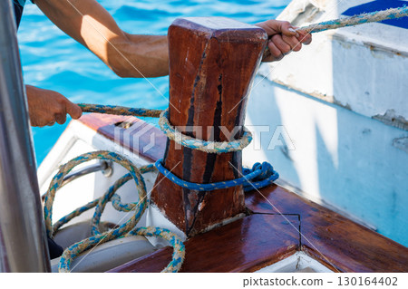Sailor securing rope on wooden cleat 130164402