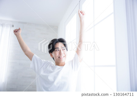 A man waking up refreshed in the morning stretching his arms by the window. Good morning. A man waking up refreshed in the morning stretching his arms by the window. Good morning. 130164711