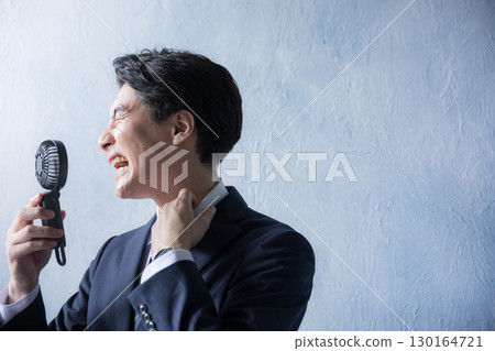 Japanese businessman suffering from the summer heat - A man in a suit using a portable fan 130164721