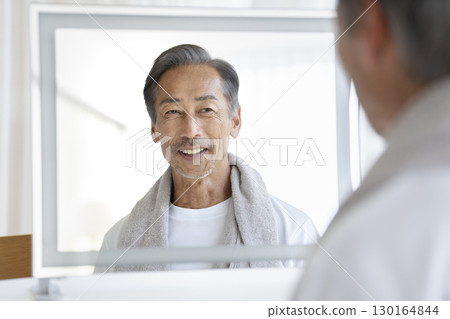 A man in his 60s smiling in the mirror. Men's beauty and health care image. 130164844