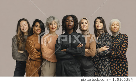 Diverse group of confident women standing together with arms crossed and smiling, showcasing unity and empowerment in neutral setting 130165394