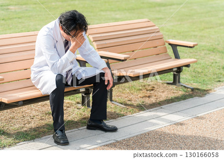 A male doctor feeling down on a park bench (worried, regretful, thinking, suffering) A male doctor feeling down on a park bench (worried, regretful, thinking, suffering) 130166058