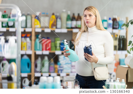 Thoughtful pregnant woman choosing kitchen degreaser spray in store 130166340