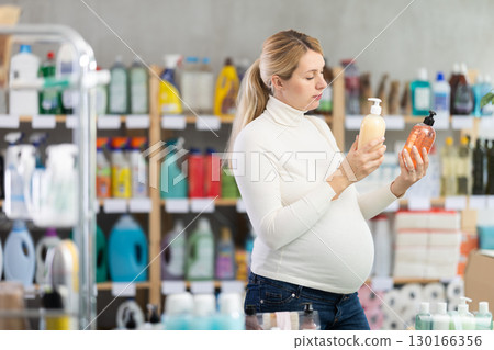 Interested pregnant woman choosing liquid soap in supermarket 130166356
