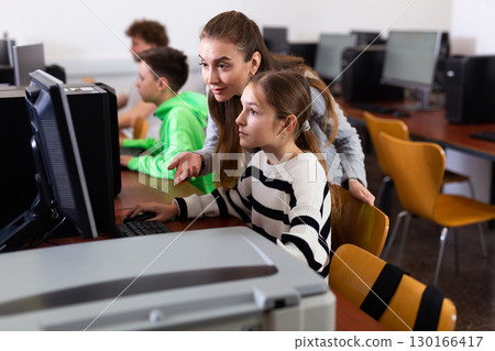 Positive woman teacher together with the girl teaches how to work on computer Positive woman teacher together with the girl teaches how to work on computer 130166417