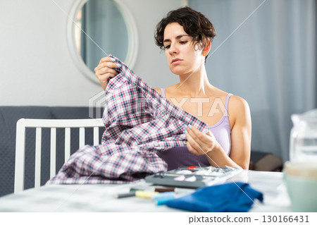 Woman sewing button on shirt sleeve at home 130166431