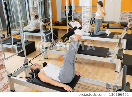 Man doing legs exercises with straps on Pilates reformer 130166451