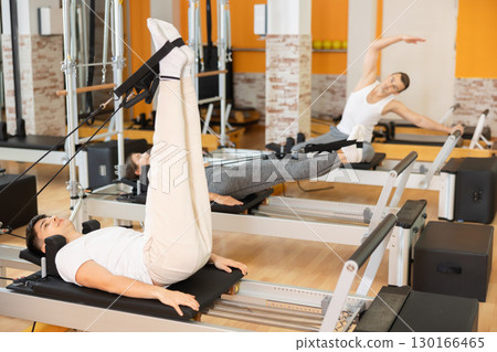 Guy performing rehabilitation feet-in-strap exercises on Pilates reformer Guy performing rehabilitation feet-in-strap exercises on Pilates reformer 130166465